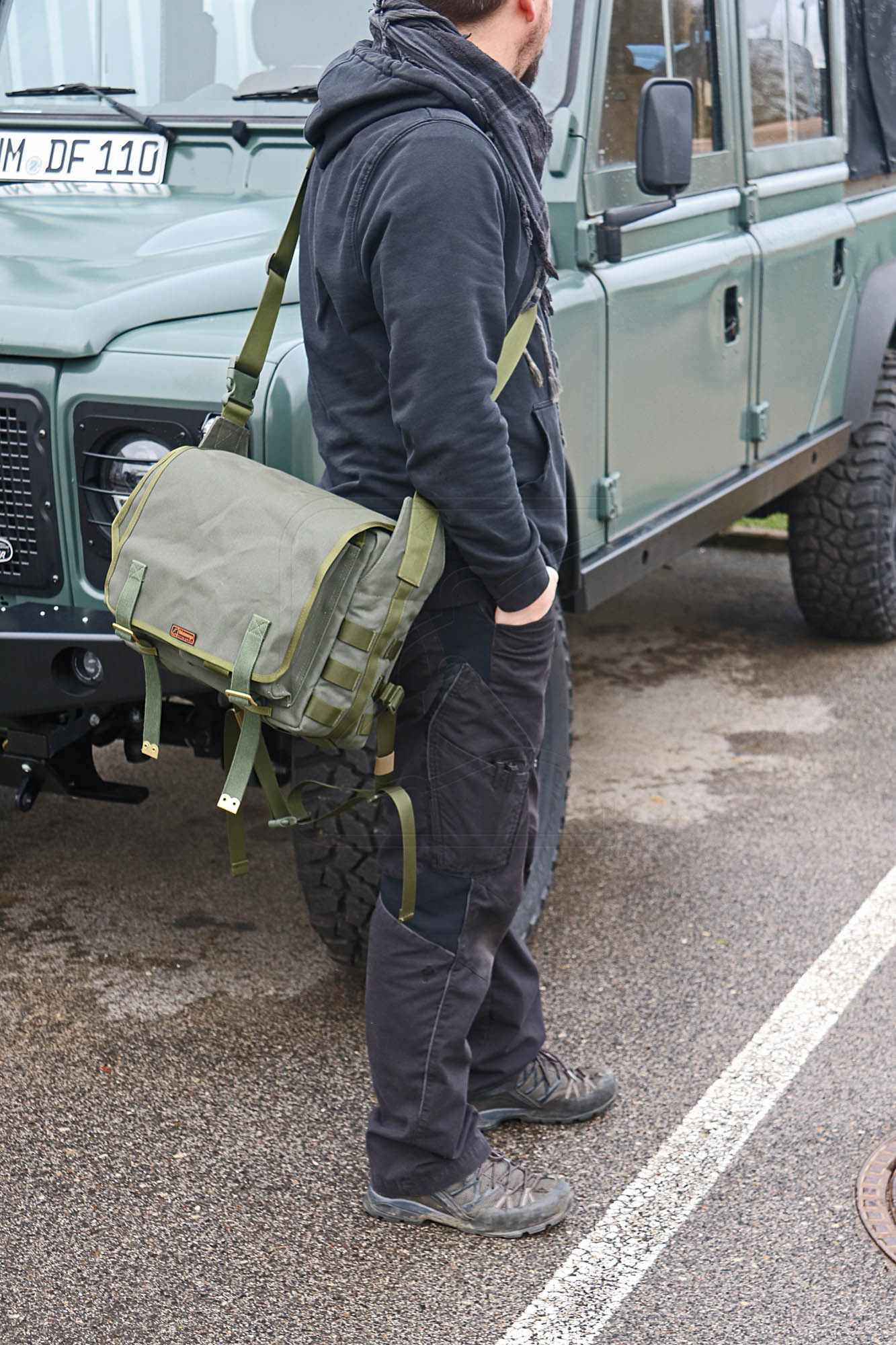 Man with olive green canvas messenger bag beside 4x4 vehicle