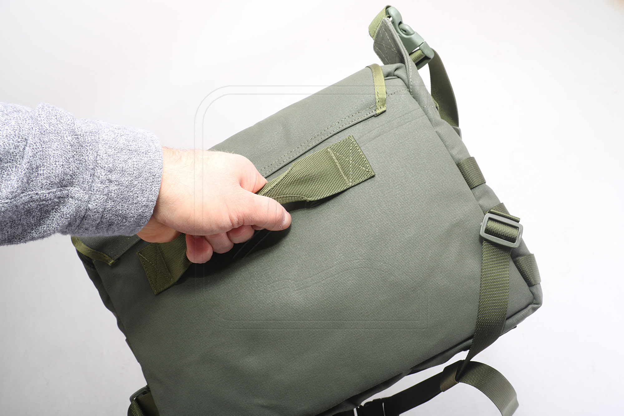 Hand holding olive green tactical backpack by grab handle